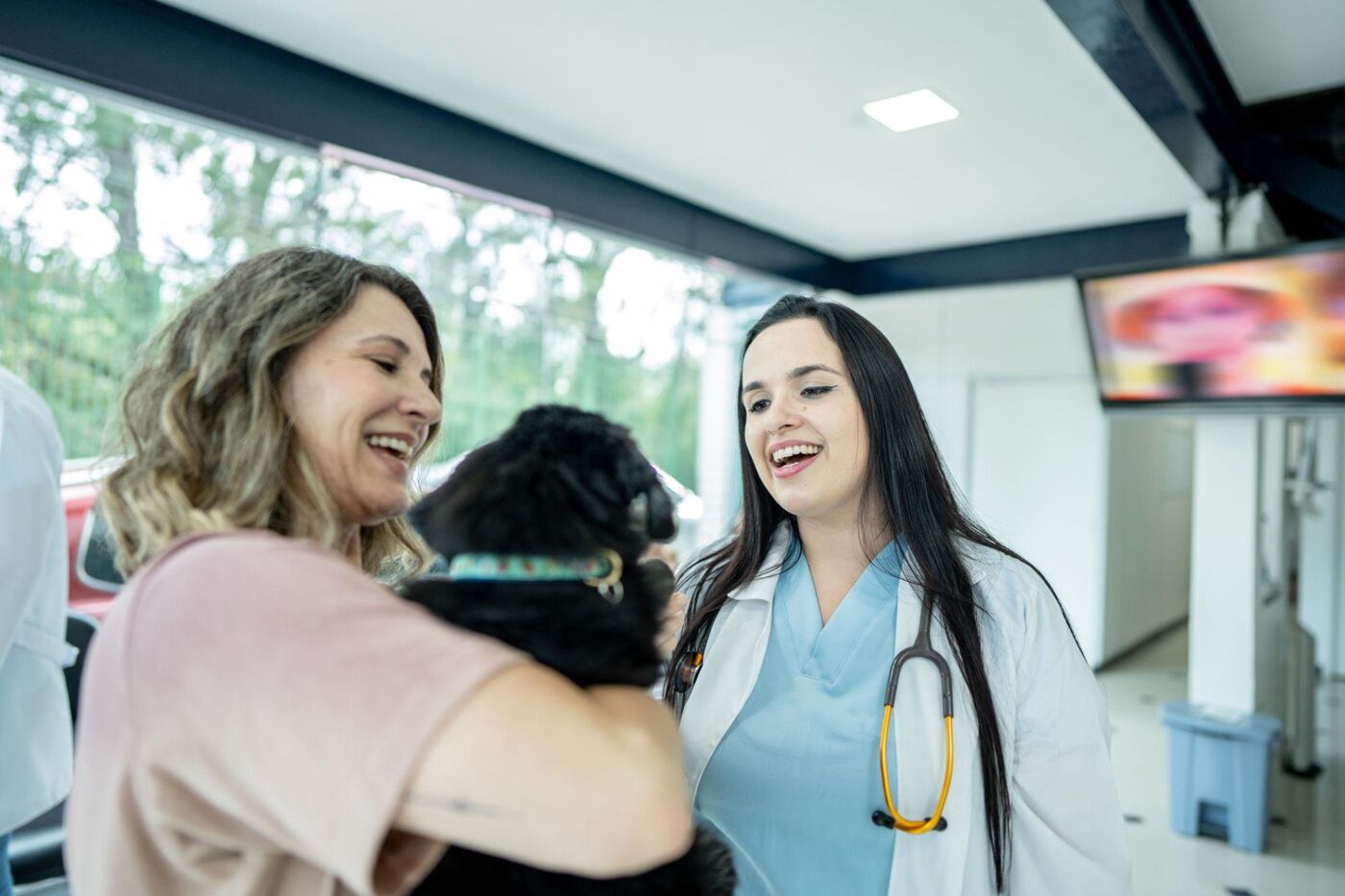 Veterinária e tutora sorrindo, cuidando de um pet juntas